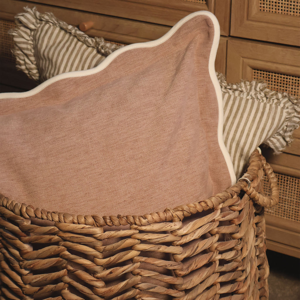 Woven basket with dusty pink scalloped cushion and striped cushion inside 