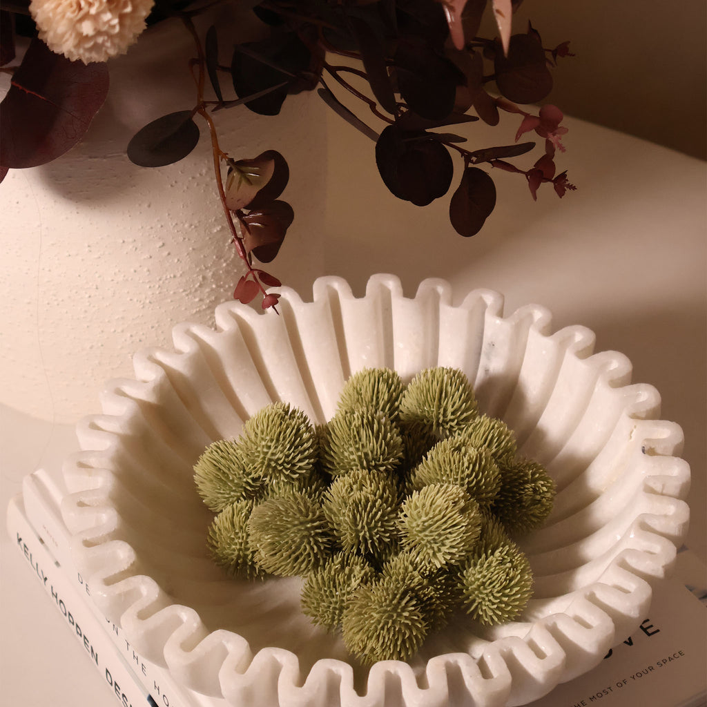 White marble fluted bowl with echinops inside on a coffee table with books, a vase and flowers