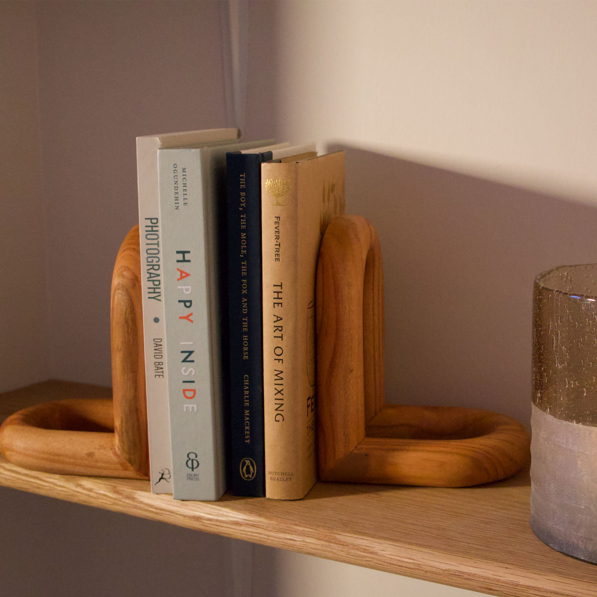 Arched wooden bookend with books and a candle holder on a shelf